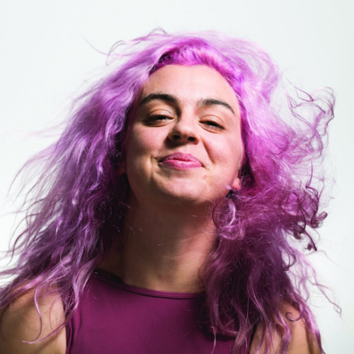 Woman with pink hair and maroon top smiling.